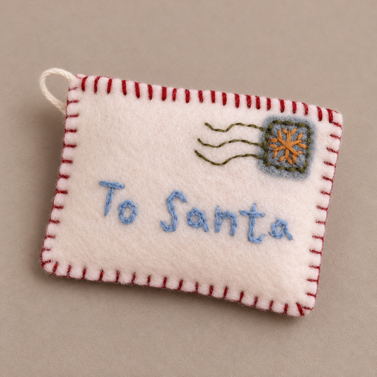 Filz-Briefanhänger Weihnachtspost mit gesticktem Schriftzug To Santa aus leicht erhöhter Perspektive vor taupefarbenem Hintergrund.
