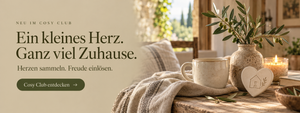 Cosy Club: Herzen sammeln und Freude einlösen – gemütliche Wohnszene mit Keramik, Kerzenlicht und einem Herz mit Hausmotiv.