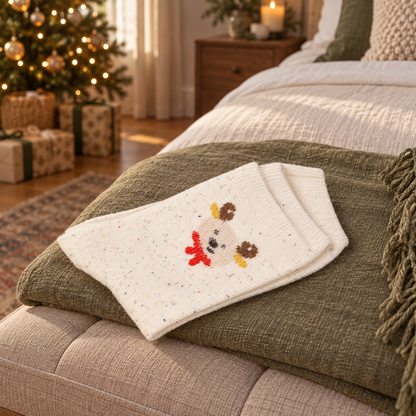 Dicke Rentiersocken „Winterfreund“ Creme 36–41 auf einer olivfarbenen Decke im weihnachtlichen Schlafzimmer