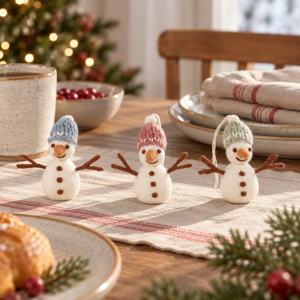 Drei Filz-Schneemänner Schneefreunde mit blauen, rosa und grünen Mützen auf einem gemütlich gedeckten Tisch.