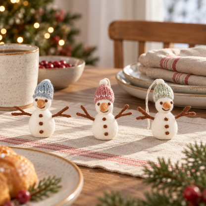 Drei Filz-Schneemänner Schneefreunde mit blauen, rosa und grünen Mützen auf einem gemütlich gedeckten Tisch.