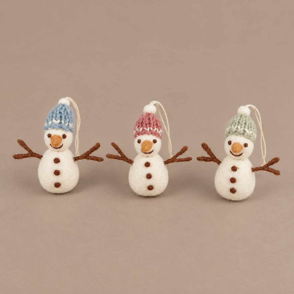 Drei Filz-Schneemänner Schneefreunde mit blauen, rosa und grünen Mützen aus leicht erhöhter Perspektive vor taupefarbenem Hintergrund.