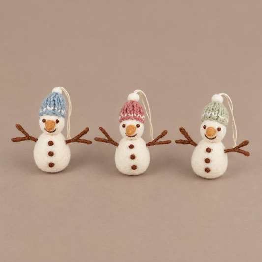 Drei Filz-Schneemänner Schneefreunde mit blauen, rosa und grünen Mützen aus leicht erhöhter Perspektive vor taupefarbenem Hintergrund.