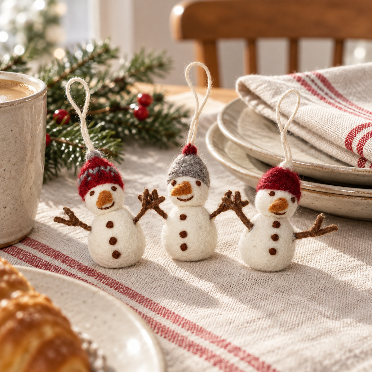 Drei Filz-Schneemänner Winterfreunde mit roten und grauen Mützen auf einem gemütlich gedeckten Tisch.