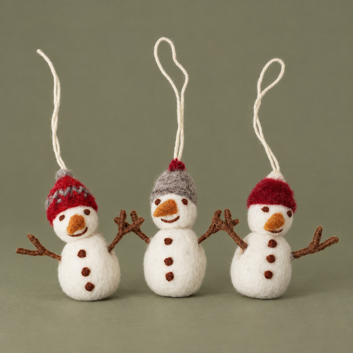 Drei Filz-Schneemänner Winterfreunde mit roten und grauen Mützen vor gedecktem olivgrauem Hintergrund.