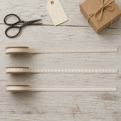 Drei cremefarbene 10-mm-Dekobänder mit weißen Linien und Herzen im Flatlay