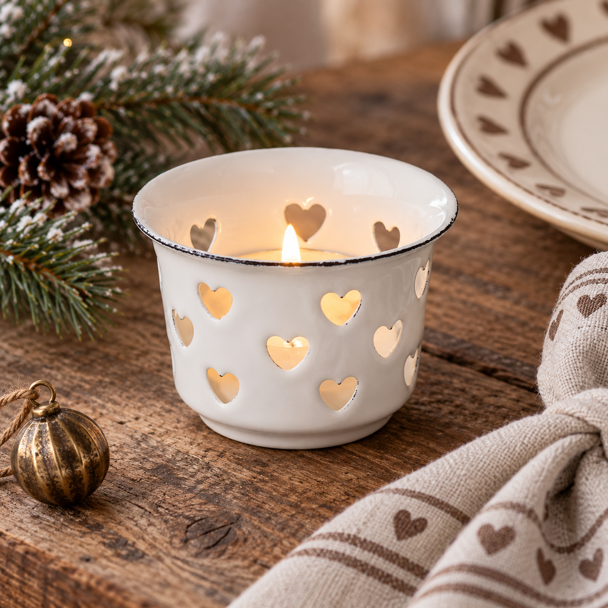 Weißer Emaille-Teelichthalter Candle Kiss mit Herzausschnitten im Detail auf einem winterlich dekorierten Holztisch