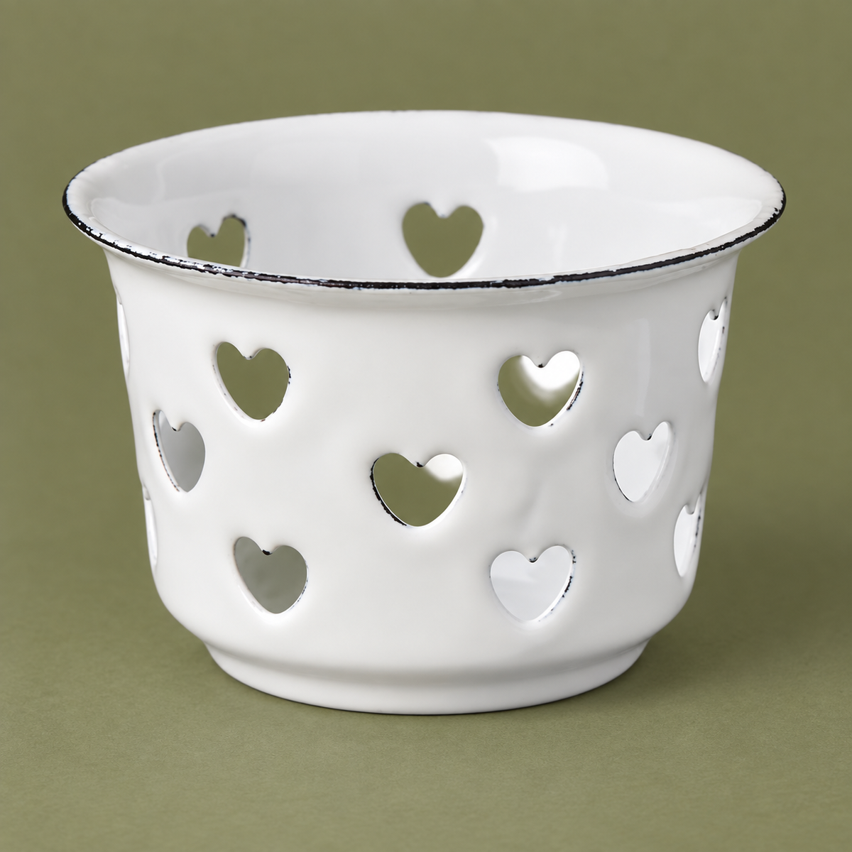 Weißer Emaille-Teelichthalter Candle Kiss mit Herzausschnitten in naher Ansicht vor einem gedeckten Naturton