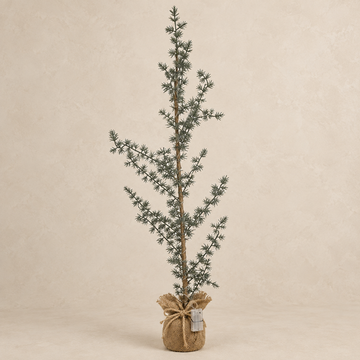 Schlanker grüner LED-Tannenbaum mit lockerem Zweigbild und naturfarbenem Sackfuß vor warmem Sandhintergrund