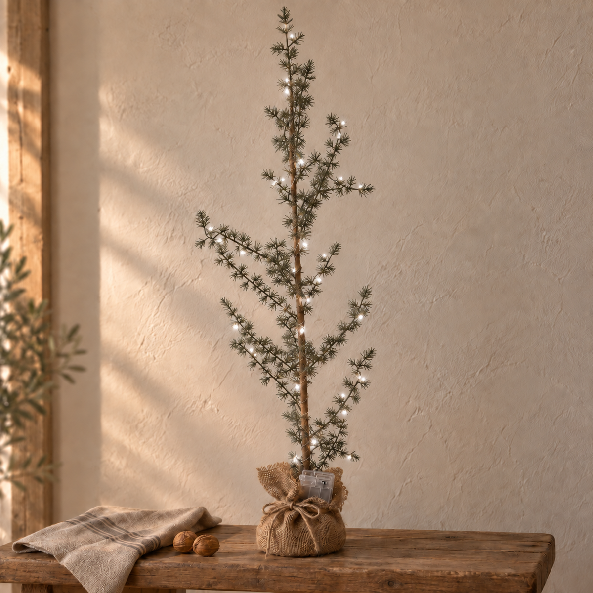 Leuchtender LED-Tannenbaum auf einer rustikalen Holzbank mit Leinen und Walnüssen