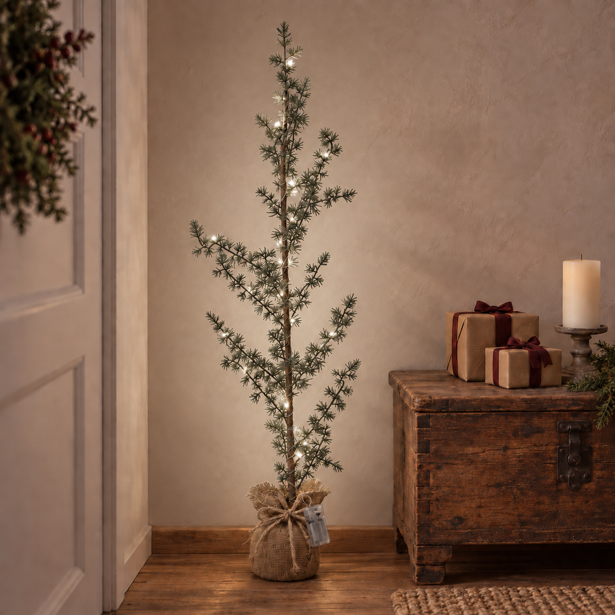LED-Tannenbaum im Sackfuß neben einer alten Holztruhe und weihnachtlich verpackten Geschenken